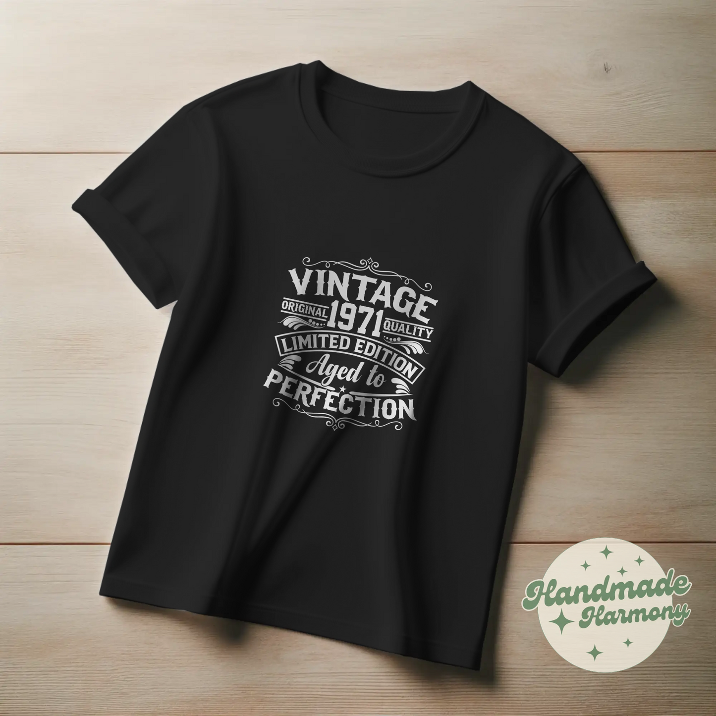 Black t-shirt with white text on a wooden surface, featuring the brand 'Handmade Harmony'.