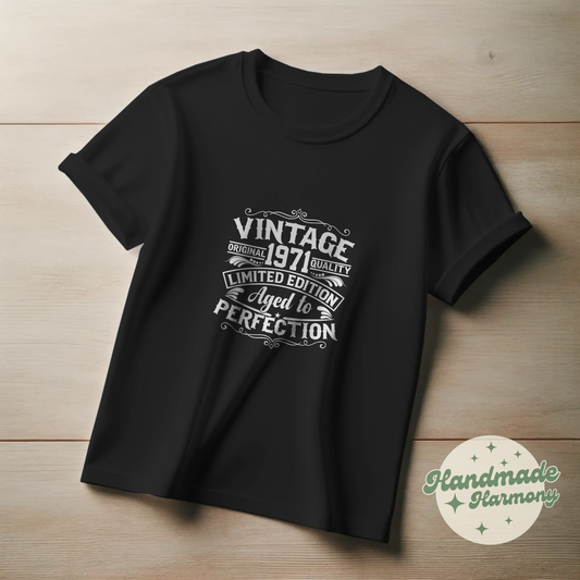 Black t-shirt with white text on a wooden surface, featuring the brand 'Handmade Harmony'.