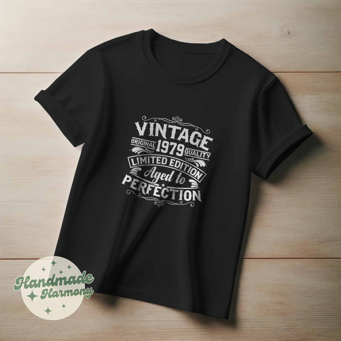 Black t-shirt with white text on a wooden surface, featuring the brand 'Handmade Harmony'.