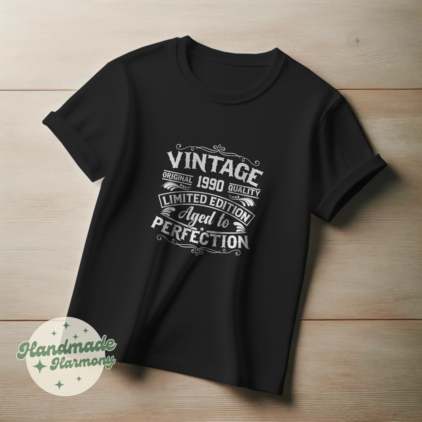 Black t-shirt with white text on a wooden surface, featuring the brand 'Handmade Harmony'.