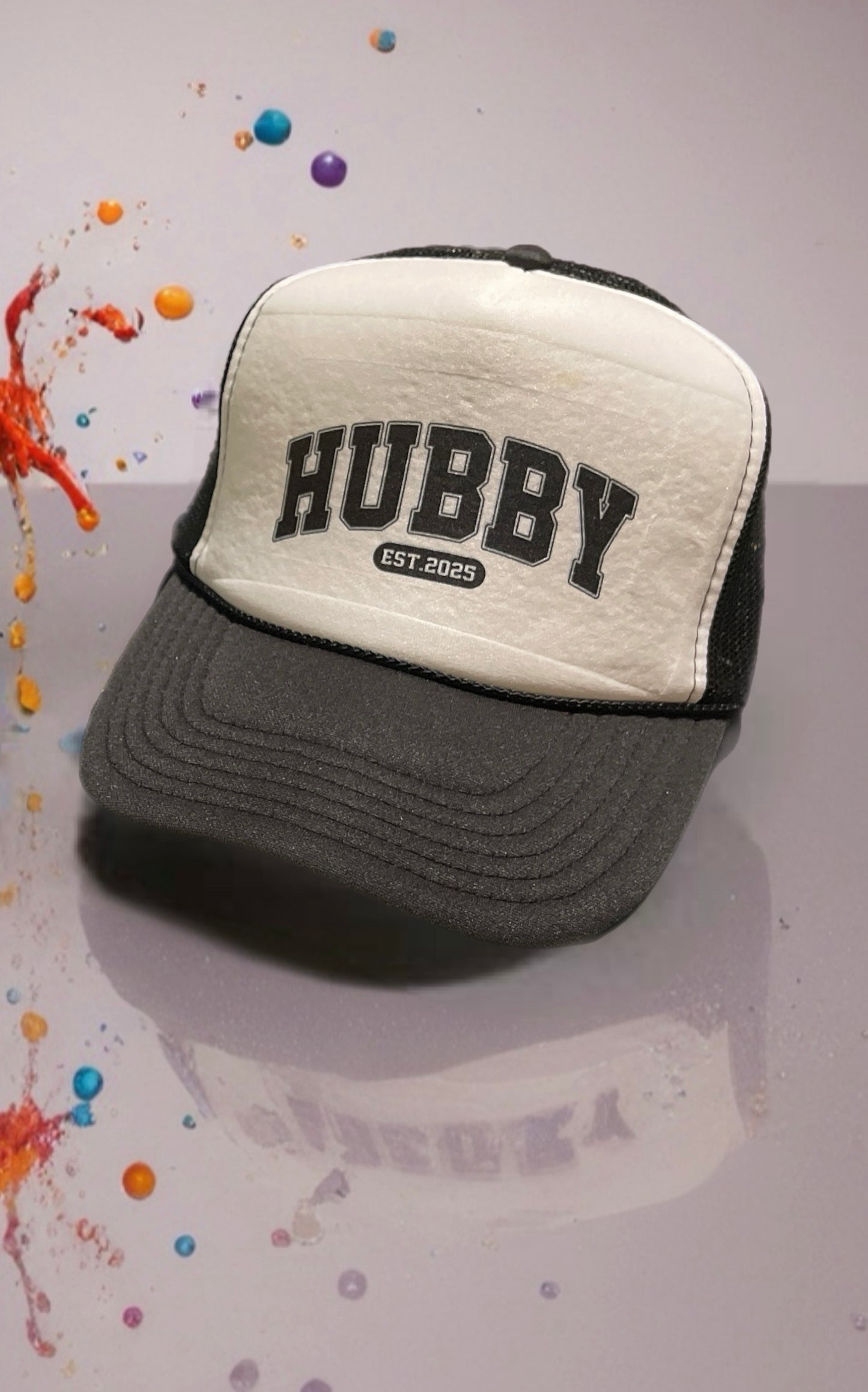Two-tone cap with 'HUBBY' text on a gray surface with colorful splashes.