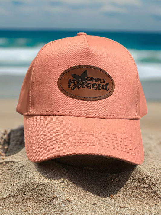 Pink cap with 'Simply Blessed' patch on a sandy beach
