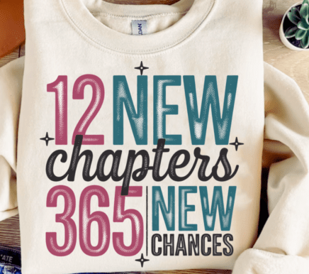 White sweatshirt with motivational text '12 New Chapters, 365 New Chances' on a wooden surface.